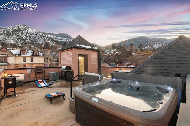 snow covered patio with cooling unit, a mountain view, and a hot tub