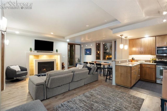 living area with a warm lit fireplace, a raised ceiling, wood finished floors, and recessed lighting