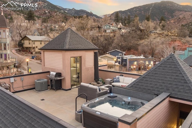 deck at dusk featuring a mountain view, central AC, a grill, an outdoor living space, and a hot tub