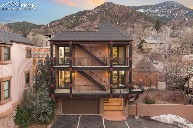 view of front of property with a mountain view, a balcony, a garage, a shingled roof, and driveway