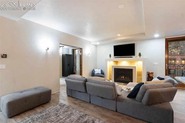 living room featuring a warm lit fireplace, light wood-style flooring, and recessed lighting