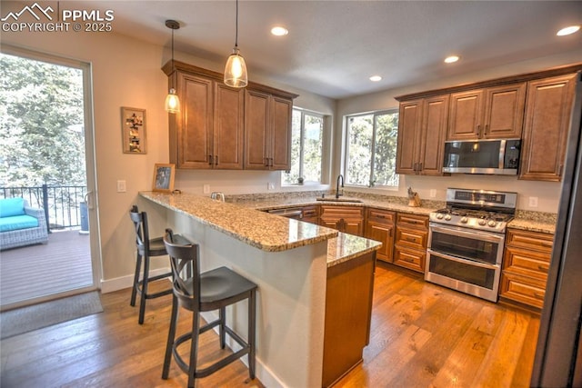 kitchen with appliances with stainless steel finishes, a kitchen breakfast bar, a peninsula, light wood-style floors, and a sink