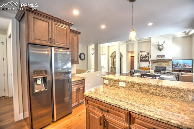 kitchen with a fireplace, stainless steel refrigerator with ice dispenser, light wood-style floors, open floor plan, and light stone countertops