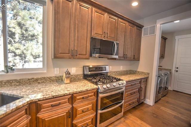 kitchen featuring visible vents, dark wood-style floors, appliances with stainless steel finishes, light stone countertops, and washing machine and dryer