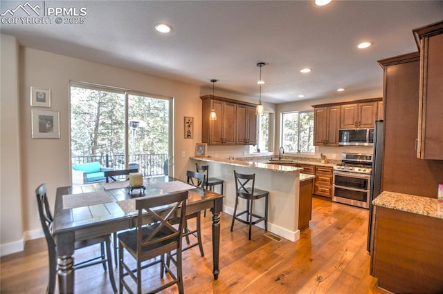 kitchen featuring a peninsula, light wood-type flooring, brown cabinets, and stainless steel appliances