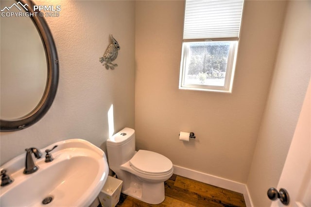 half bath with toilet, baseboards, a sink, and wood finished floors