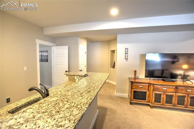 kitchen with light stone counters, light carpet, a sink, and baseboards