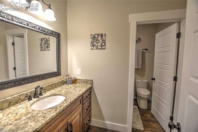 bathroom with toilet, baseboards, wood finished floors, and vanity