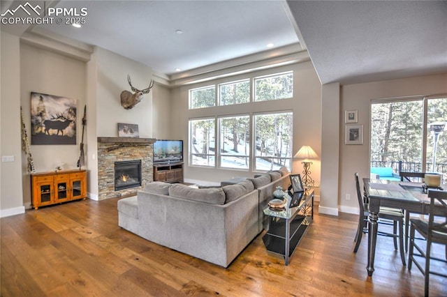 living room with a stone fireplace, recessed lighting, wood finished floors, and baseboards