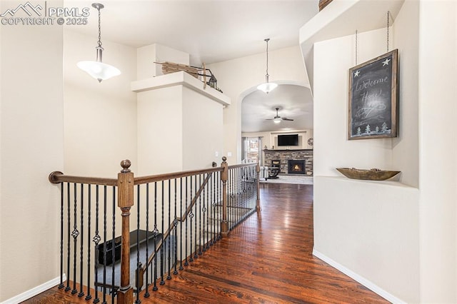 corridor featuring an upstairs landing, wood finished floors, arched walkways, and baseboards