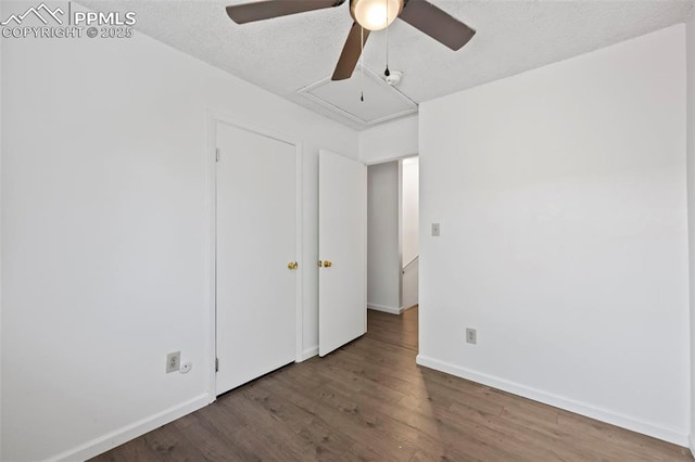 unfurnished bedroom featuring attic access, ceiling fan, a textured ceiling, wood finished floors, and baseboards