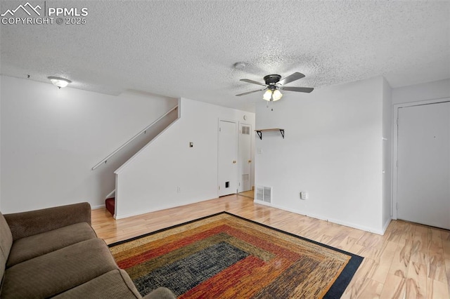 living area with a textured ceiling, ceiling fan, wood finished floors, visible vents, and stairway