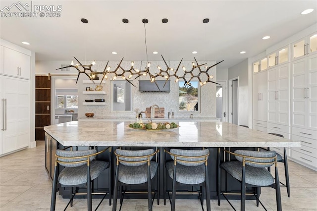 kitchen with white cabinets, a spacious island, glass insert cabinets, light stone counters, and pendant lighting