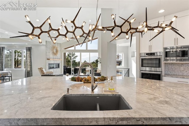 kitchen featuring stainless steel appliances, a fireplace, a sink, white cabinetry, and light stone countertops