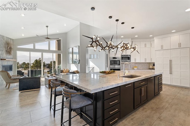 kitchen with white cabinets, a spacious island, appliances with stainless steel finishes, decorative light fixtures, and a sink