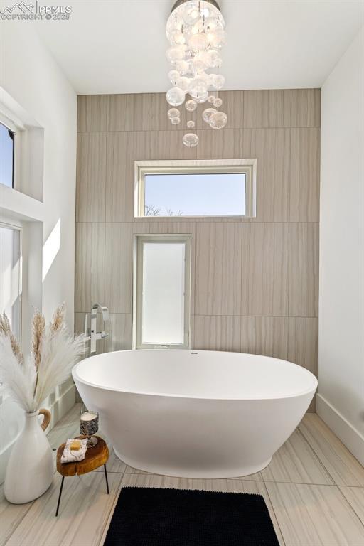 bathroom featuring a freestanding tub, a notable chandelier, and tile walls