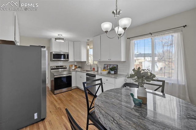 kitchen with a sink, white cabinetry, hanging light fixtures, appliances with stainless steel finishes, and light stone countertops