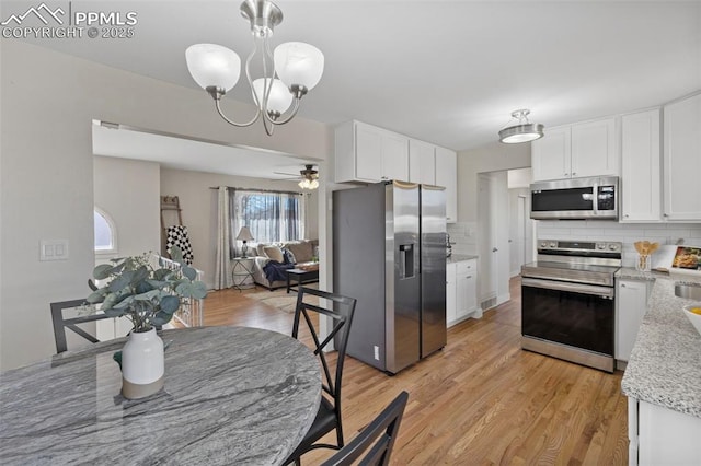 kitchen featuring stainless steel appliances, white cabinetry, hanging light fixtures, and light wood-style flooring