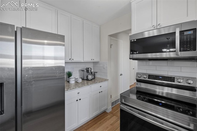 kitchen with stainless steel appliances, white cabinetry, light wood-style flooring, and light stone countertops