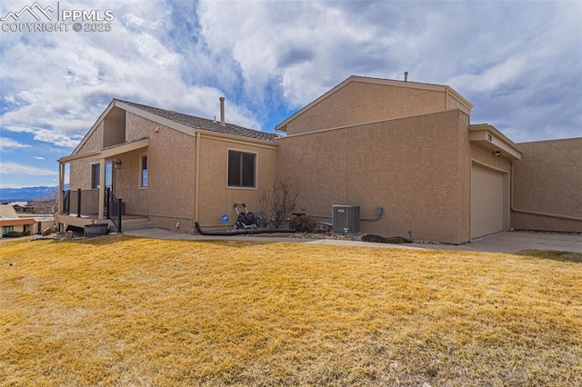 back of house with central AC unit, a lawn, an attached garage, and stucco siding