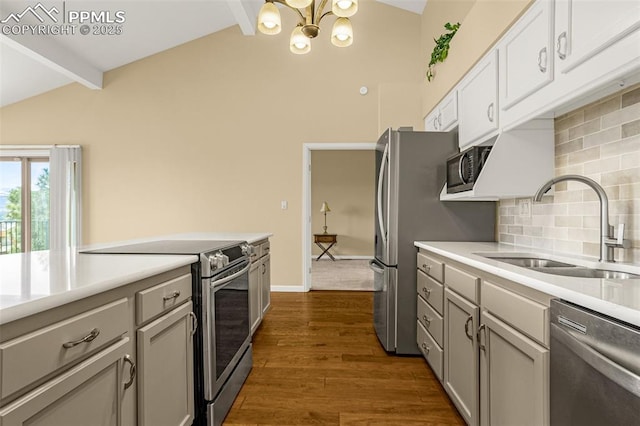 kitchen featuring dark wood-style floors, vaulted ceiling with beams, stainless steel appliances, decorative backsplash, and a sink