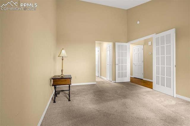 unfurnished room with french doors, carpet, a towering ceiling, and baseboards