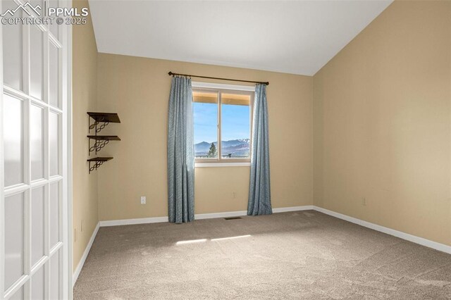 spare room featuring carpet floors, visible vents, baseboards, and lofted ceiling