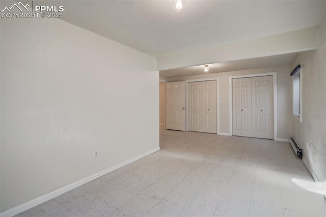 unfurnished bedroom with a baseboard heating unit, baseboards, and two closets