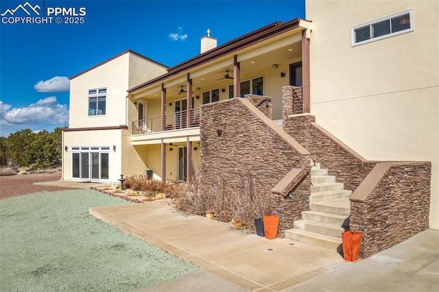 back of house with ceiling fan, a balcony, stairs, stucco siding, and a chimney