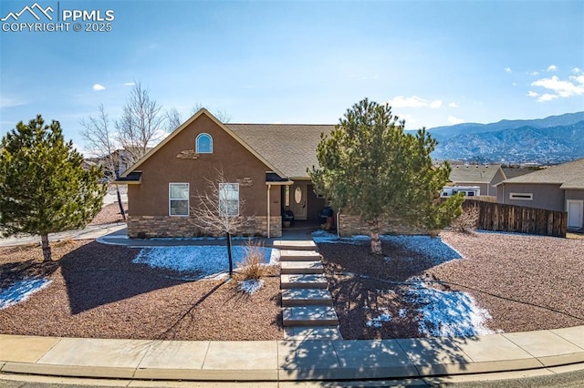 view of front of property featuring stone siding, fence, a mountain view, and stucco siding