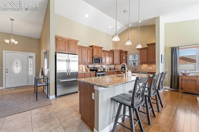 kitchen with light stone counters, a breakfast bar area, decorative light fixtures, stainless steel appliances, and a center island with sink