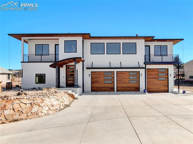 contemporary home featuring a garage, a balcony, driveway, and stucco siding