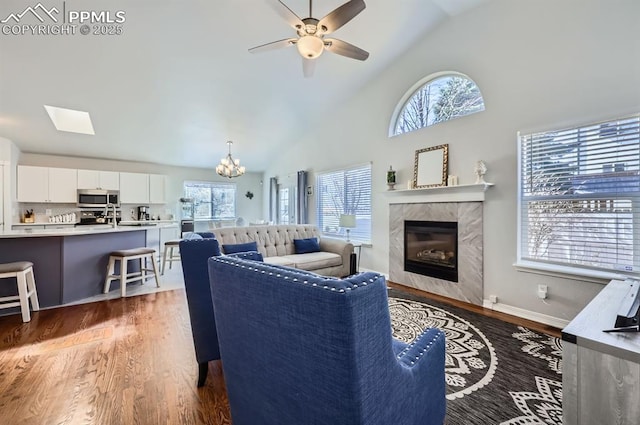 living area with ceiling fan with notable chandelier, a high end fireplace, baseboards, and wood finished floors