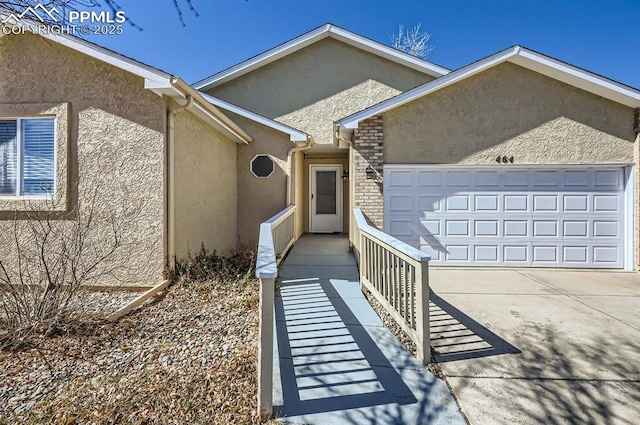 doorway to property featuring a garage, brick siding, driveway, and stucco siding