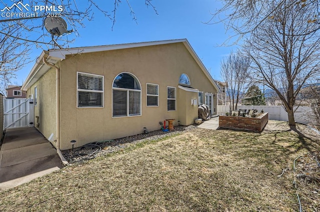 rear view of property with fence, a lawn, and stucco siding