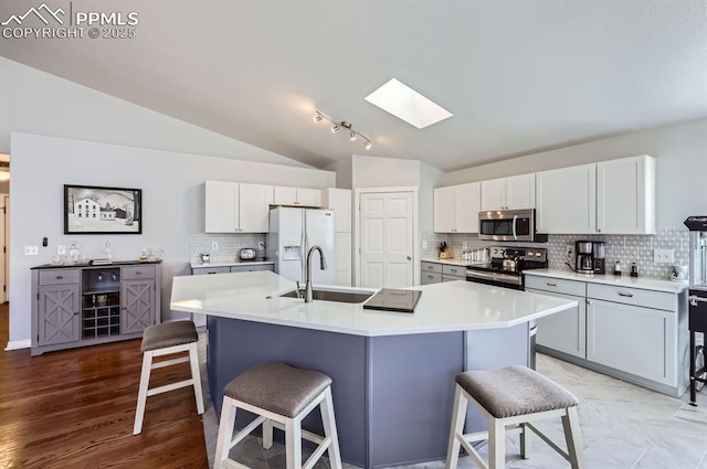 kitchen featuring a sink, light countertops, appliances with stainless steel finishes, lofted ceiling with skylight, and a kitchen bar