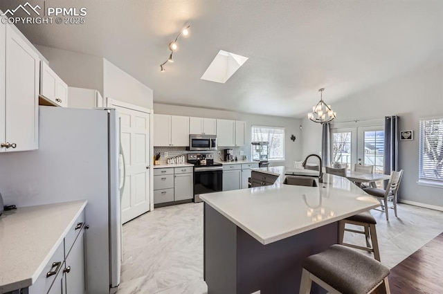 kitchen featuring vaulted ceiling with skylight, a breakfast bar, range with electric stovetop, a sink, and stainless steel microwave