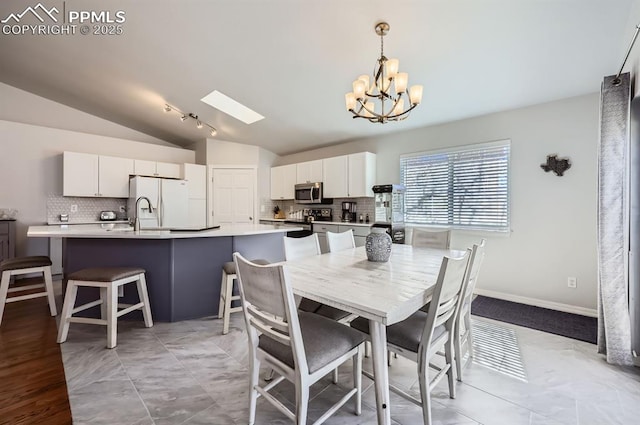 dining space with a chandelier, vaulted ceiling with skylight, and baseboards