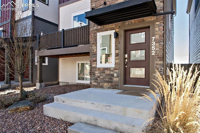 view of exterior entry with stone siding and a balcony