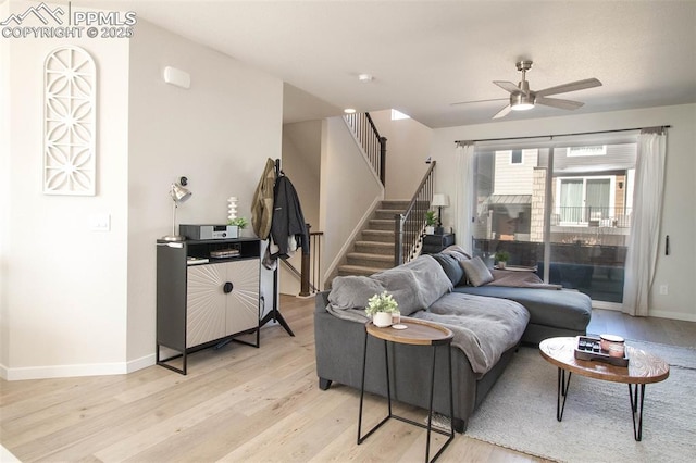 living area featuring light wood-style flooring, stairway, baseboards, and a ceiling fan