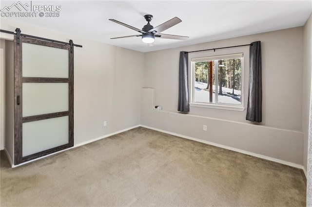 empty room with a barn door, baseboards, a ceiling fan, and carpet flooring