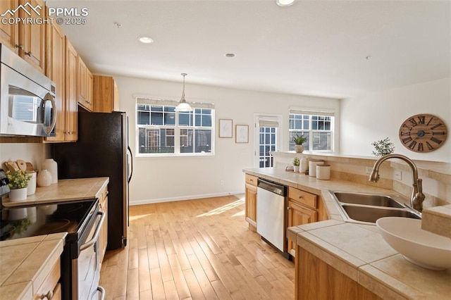 kitchen featuring tile countertops, a sink, light wood-style floors, appliances with stainless steel finishes, and pendant lighting