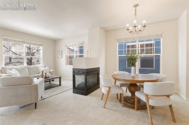 dining room with carpet floors, baseboards, a chandelier, and a multi sided fireplace