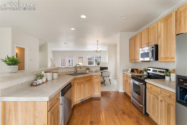 kitchen with stainless steel appliances, light brown cabinetry, a sink, and pendant lighting