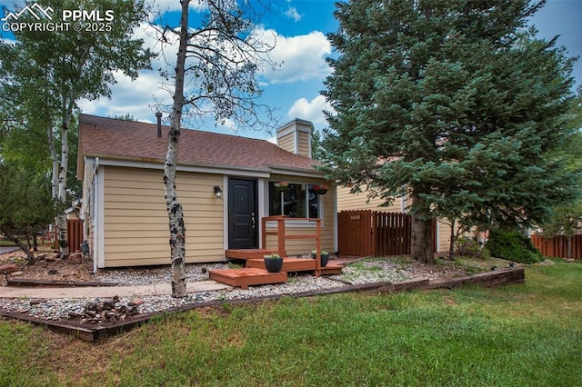 rear view of property with roof with shingles, a chimney, fence, and a yard