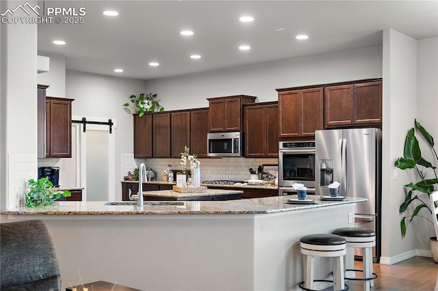 kitchen featuring a barn door, appliances with stainless steel finishes, backsplash, light stone counters, and a sink