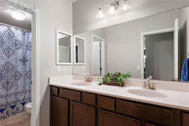 full bath with toilet, a shower with curtain, double vanity, and a sink