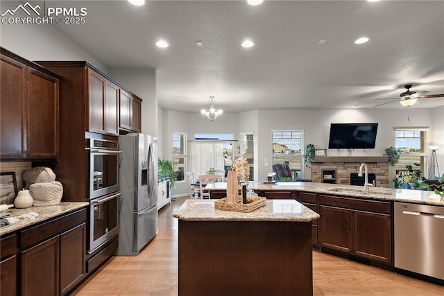 kitchen featuring a fireplace, stainless steel appliances, light wood-style flooring, a sink, and a kitchen island