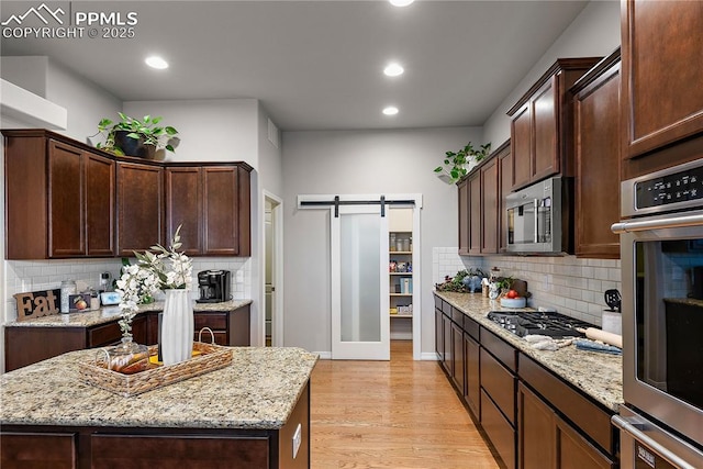 kitchen featuring light wood finished floors, a barn door, a kitchen island, appliances with stainless steel finishes, and light stone countertops