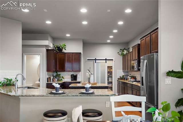 kitchen featuring light stone countertops, a barn door, appliances with stainless steel finishes, and a sink